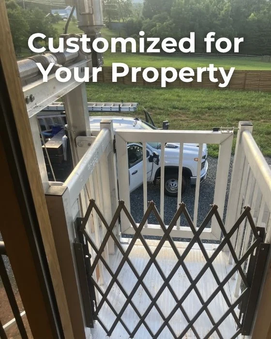 Outdoor home elevator with safety gate, customized for properties. White truck visible on gravel driveway, green lawn beyond.