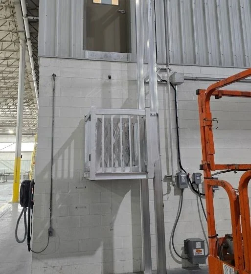 Industrial setting with a small, metal home elevator system attached to a brick and metal wall, near electrical wiring.