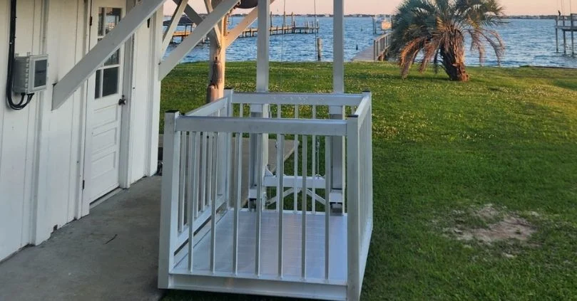 Outdoor white home elevator set against a grassy yard with a palm tree and a distant view of a lake and dock in the background.