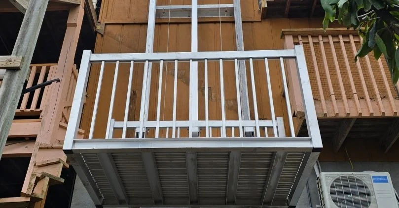 Outdoor platform lift with metal railing, part of home elevators setup, installed between wooden structures.