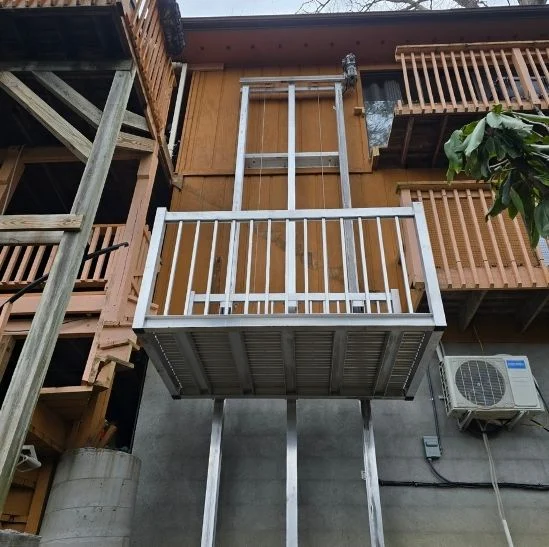 Exterior view of a wooden building with a metal platform, possibly home elevators, next to a mounted air conditioning unit.